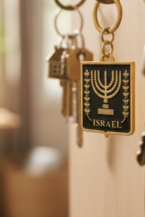 A small clear plastic bag containing a black and gold Israel-themed keychain or charm, placed on top of a black laptop keyboard.